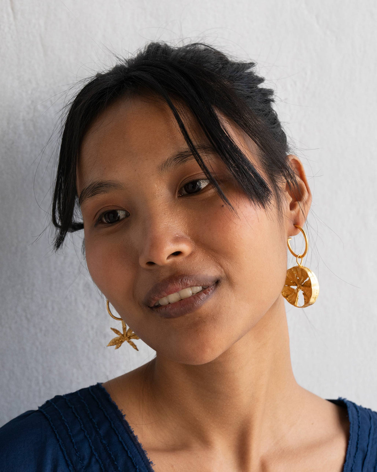 Person wearing gold hoop earrings with a round disc drop.