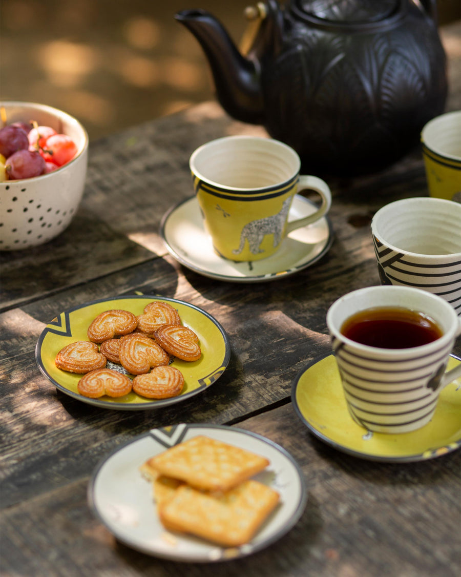 Leopard tea plates with biscuits beside a black teapot and cups outdoors