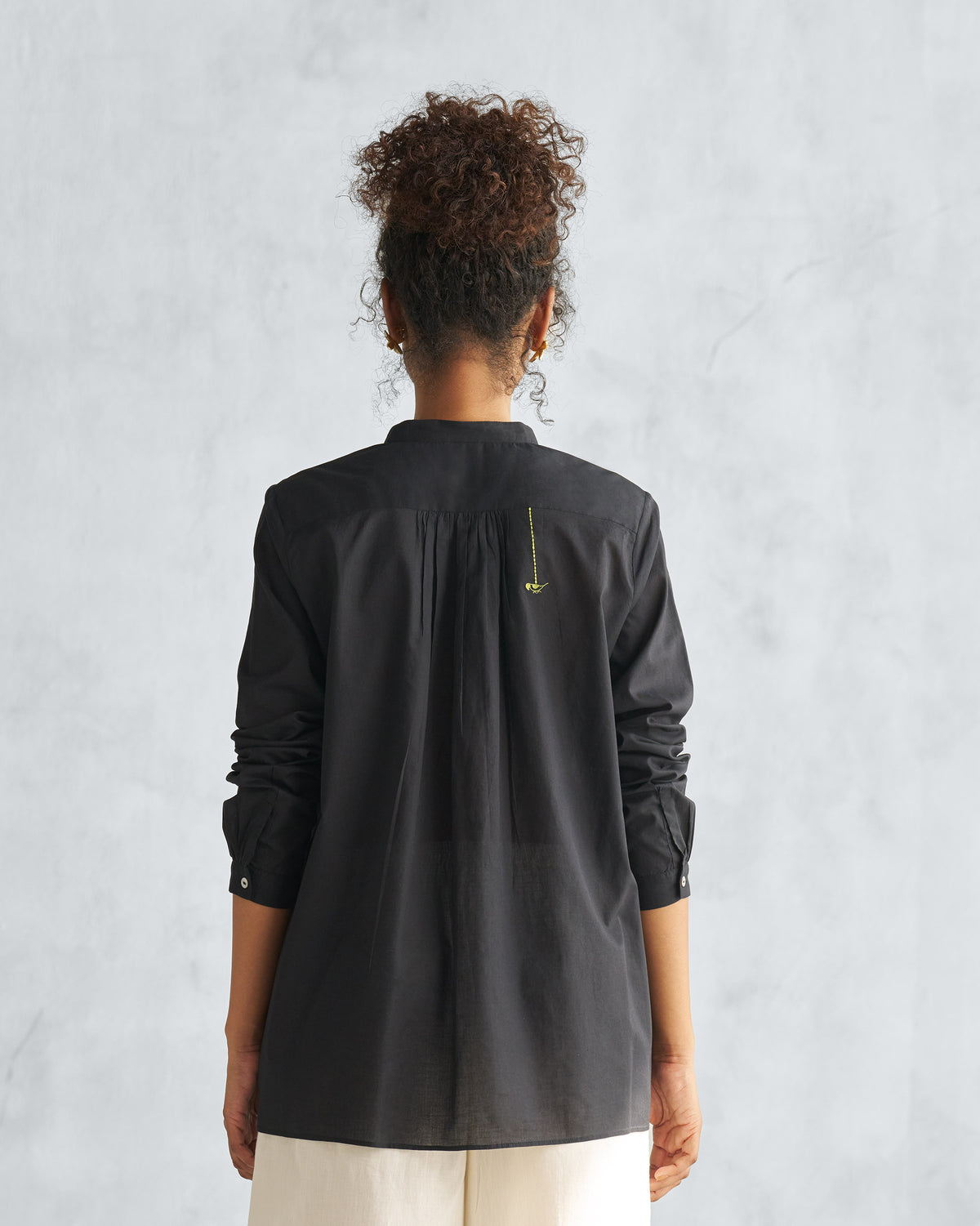 Back of a black mandarin collar top with a gathered yoke.