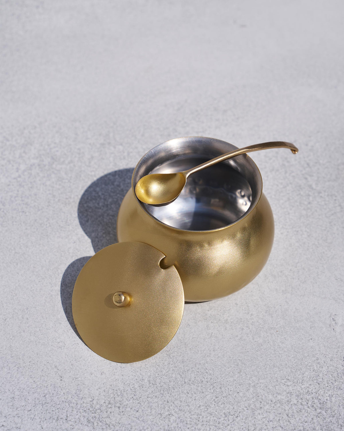 Open Madhu ghee pot showing silver interior with lid and ladle beside it.