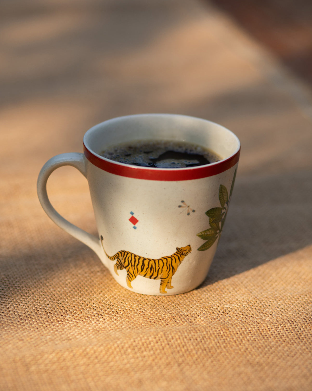 Nadi conical mug showing a walking tiger print beside green leaves and a red rim.