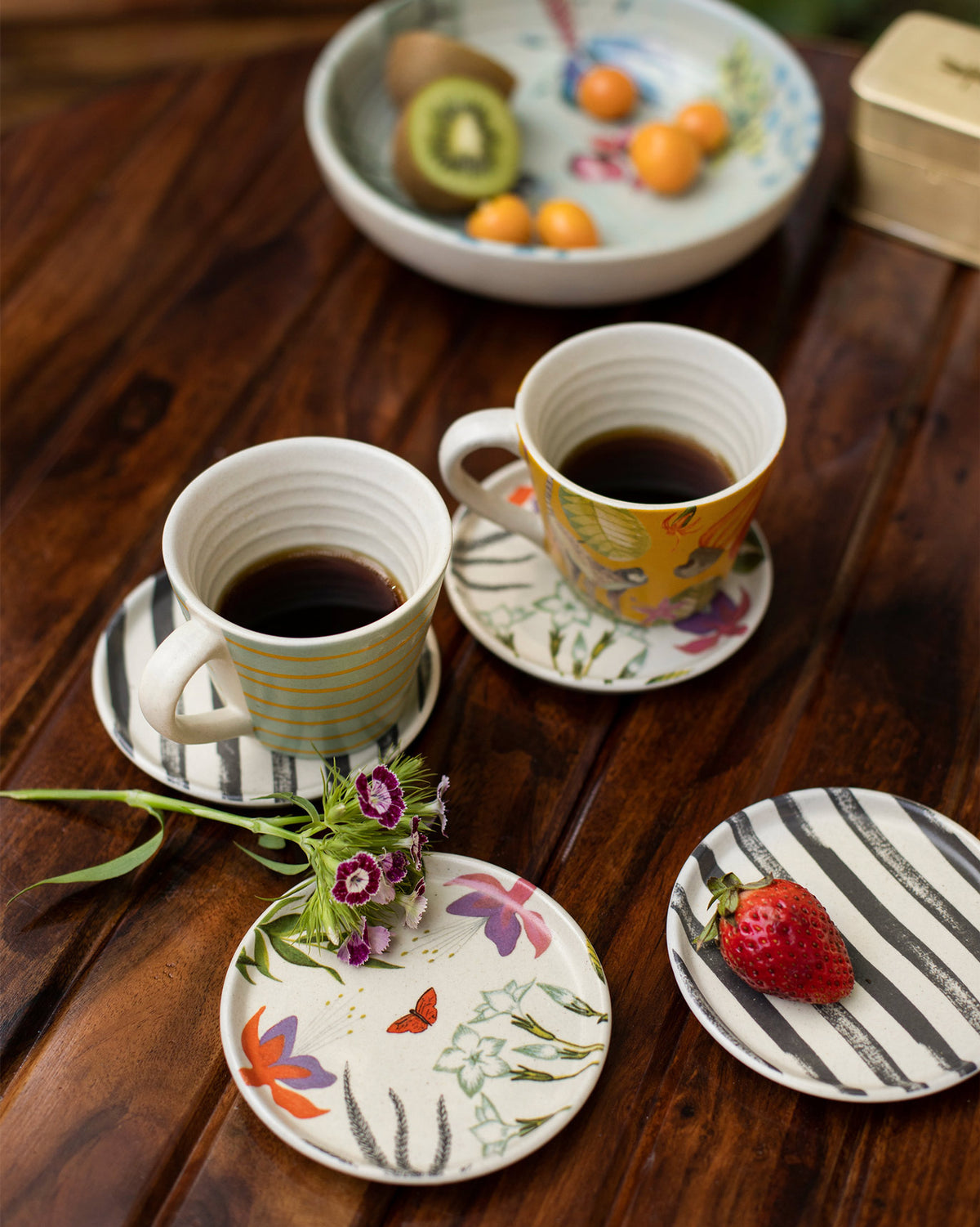 Botanical coasters under coffee mugs, showing stripe and floral designs on wood.