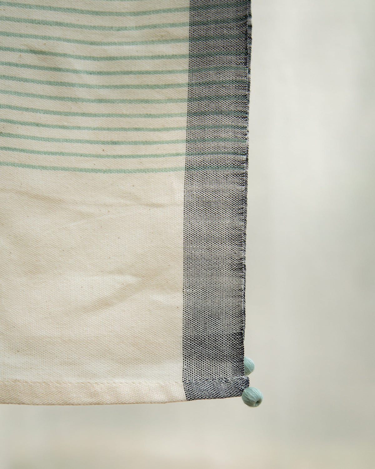 Close-up of Coast Towel corner showing its aqua stripes and pom-pom tassel.