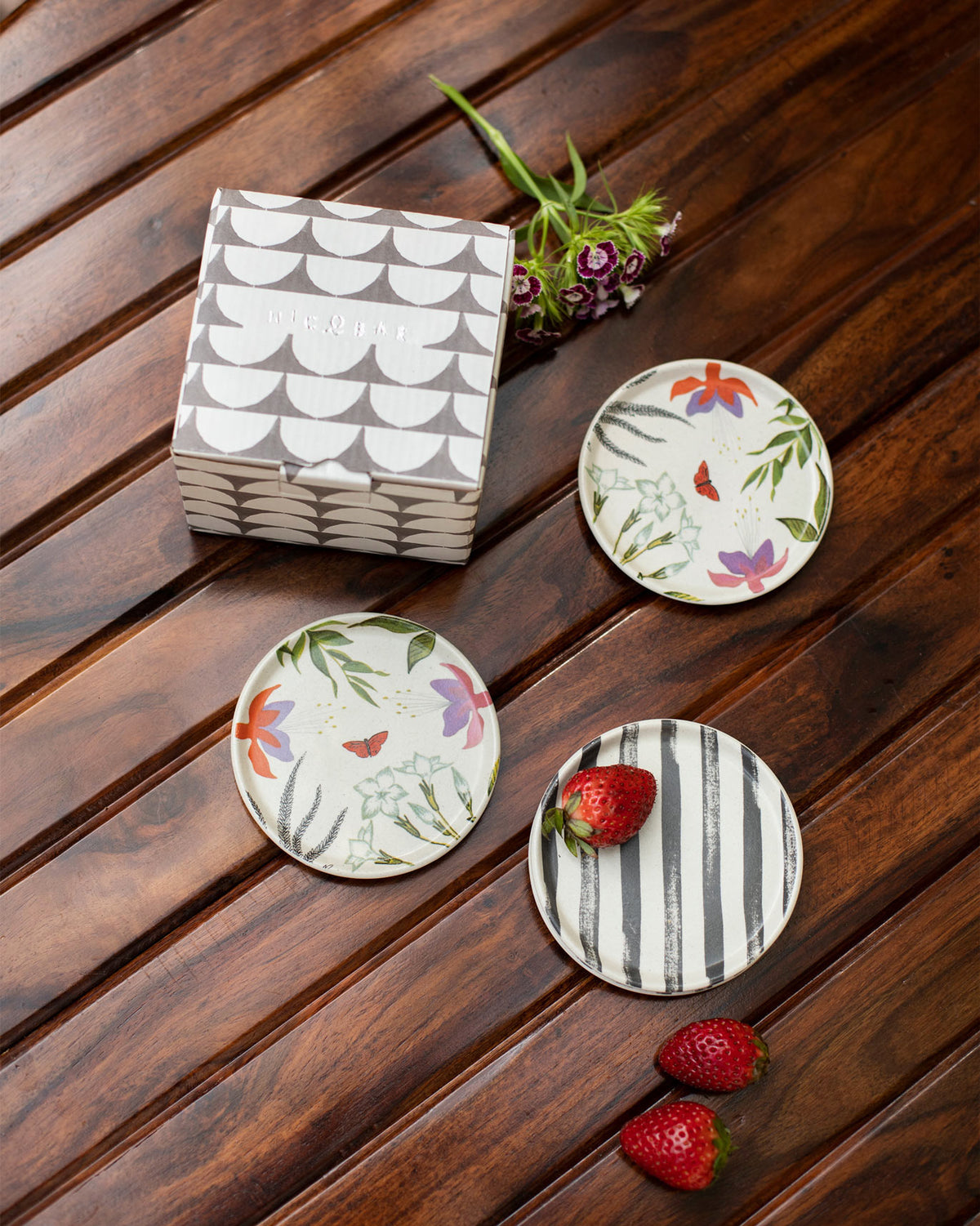 Botanical coasters with floral and stripe prints beside a Nicobar gift box.