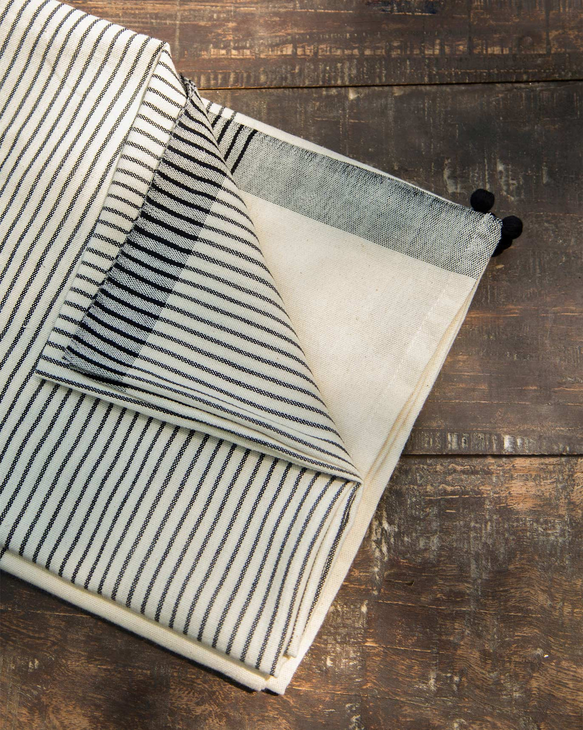 Folded Coast Towel in black stripes with pom-pom ends.
