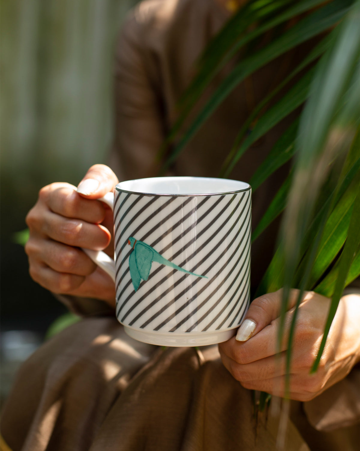 Person holding a striped Tota Mug with a teal bird.