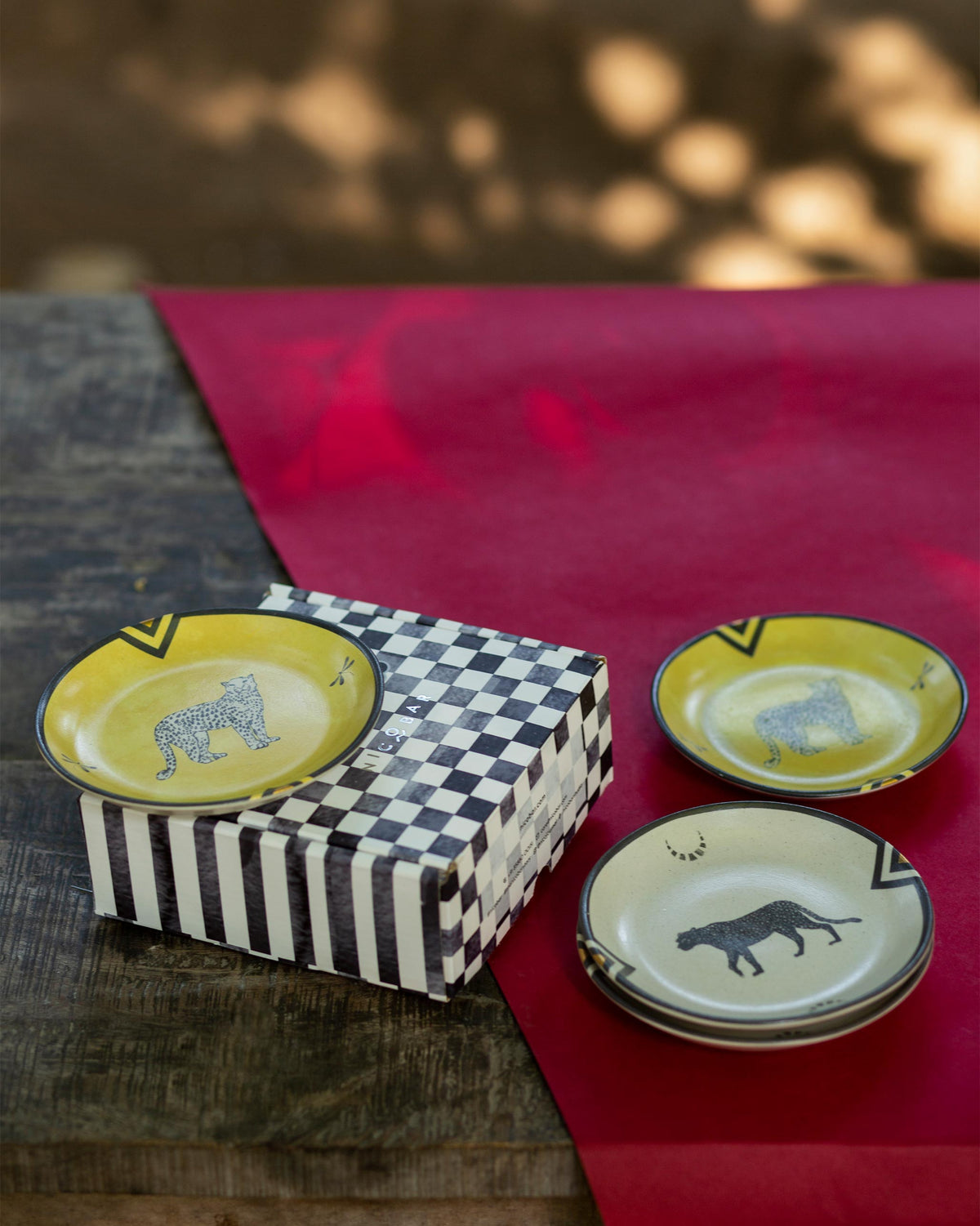 Leopard Tea Plates in yellow and cream with leopard motifs, beside a checkered box.