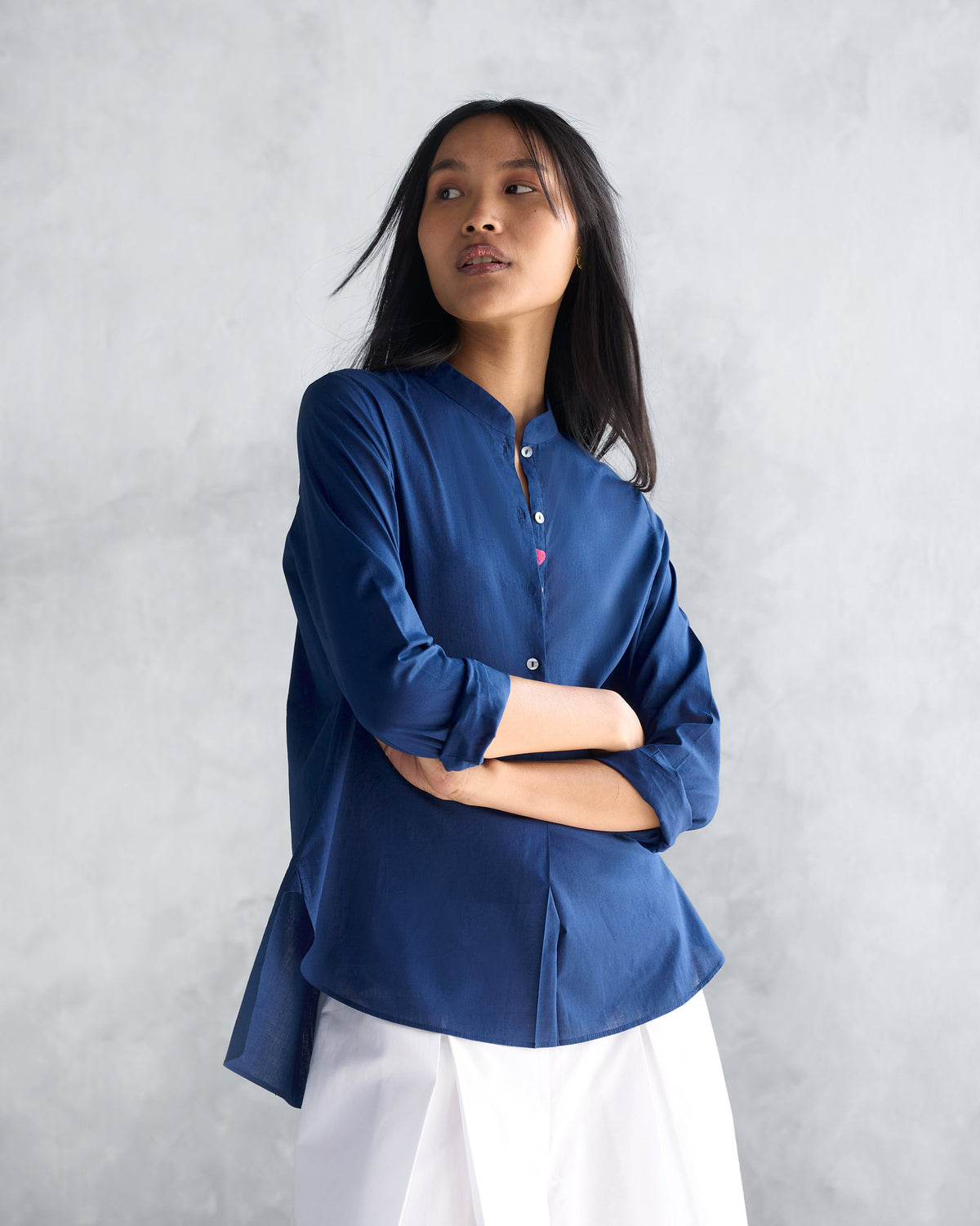 Person wearing a navy mandarin collar top with its sleeves pushed up.