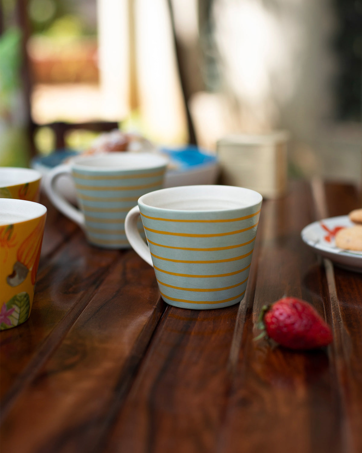 Blue Mahi espresso mug with thin yellow stripes on a wooden table.