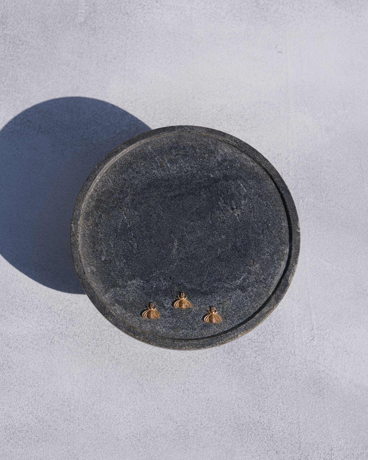 Overhead of a Firefly cake stand top with three gold fireflies on dark marble.