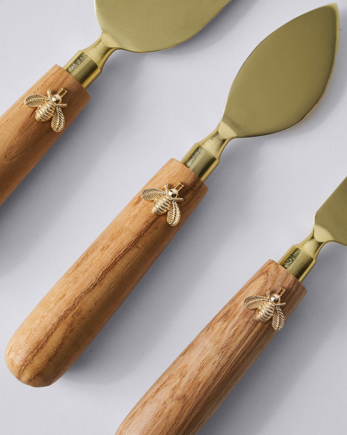 Close-up of Garo cheese knife handles with brass bee charms on natural wood.