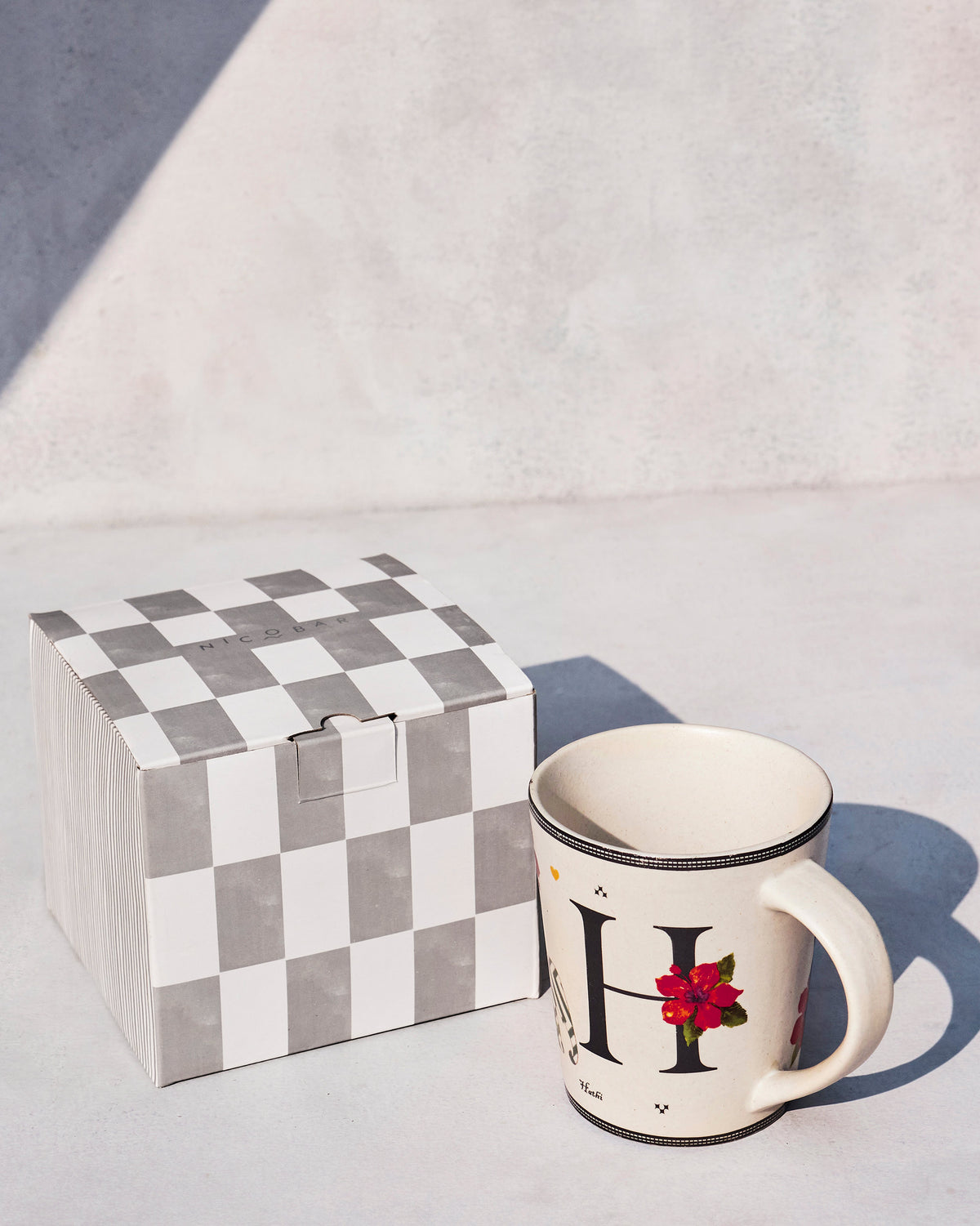 Hans mug with letter H and a hibiscus beside a checkered Nicobar gift box.