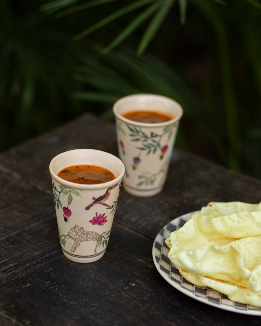 Two Nakano kulhars of soup beside papad on a dark table among plants