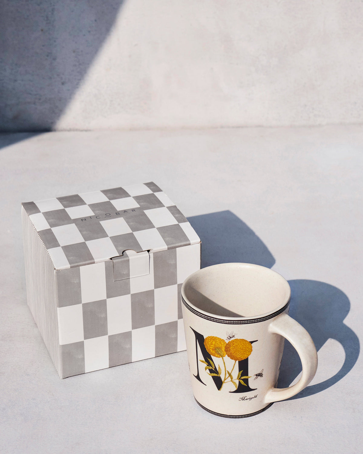 Marigold alphabet mug beside a checkered Nicobar gift box.