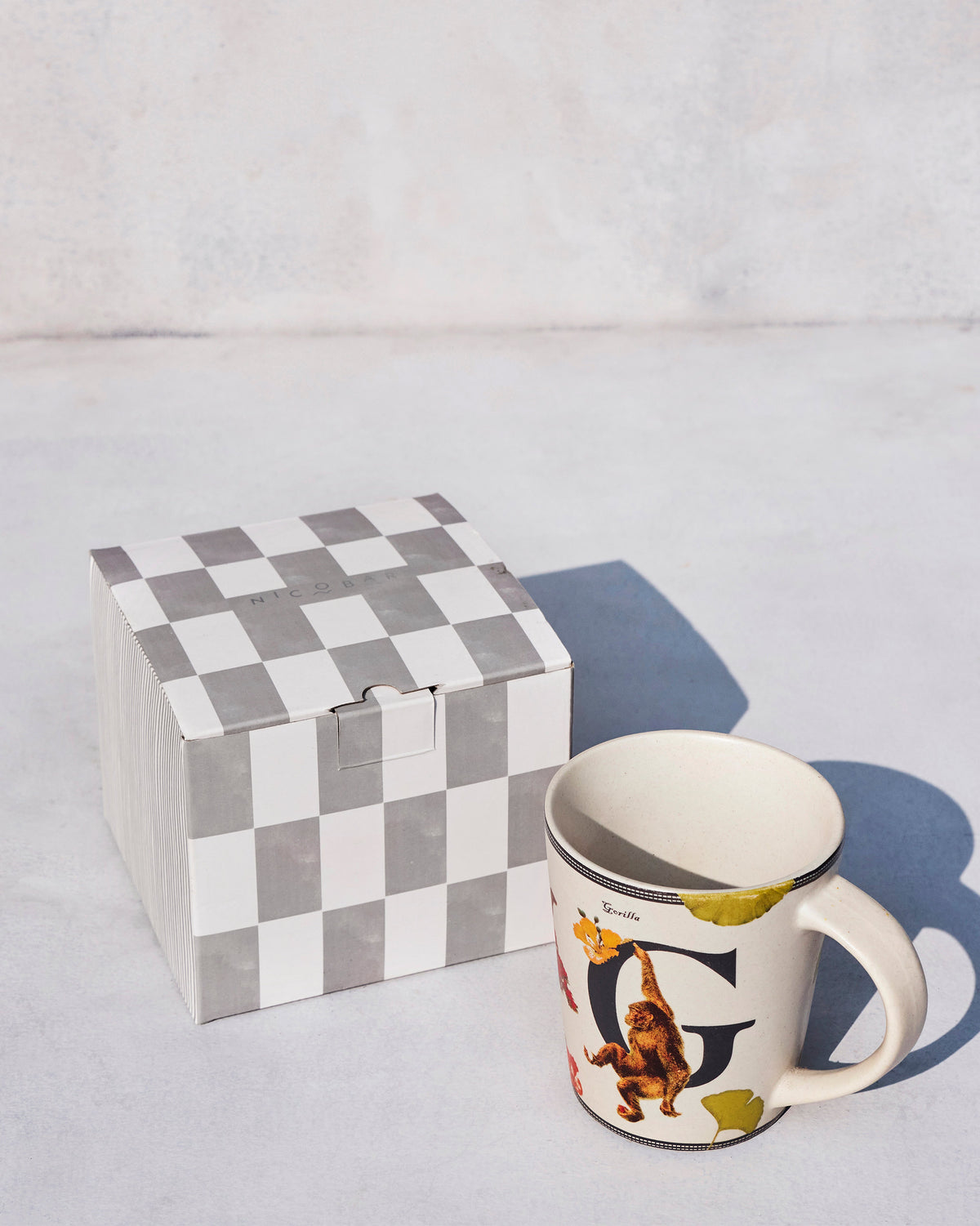 Gulmohar mug with letter G and gorilla beside a checkered Nicobar gift box.