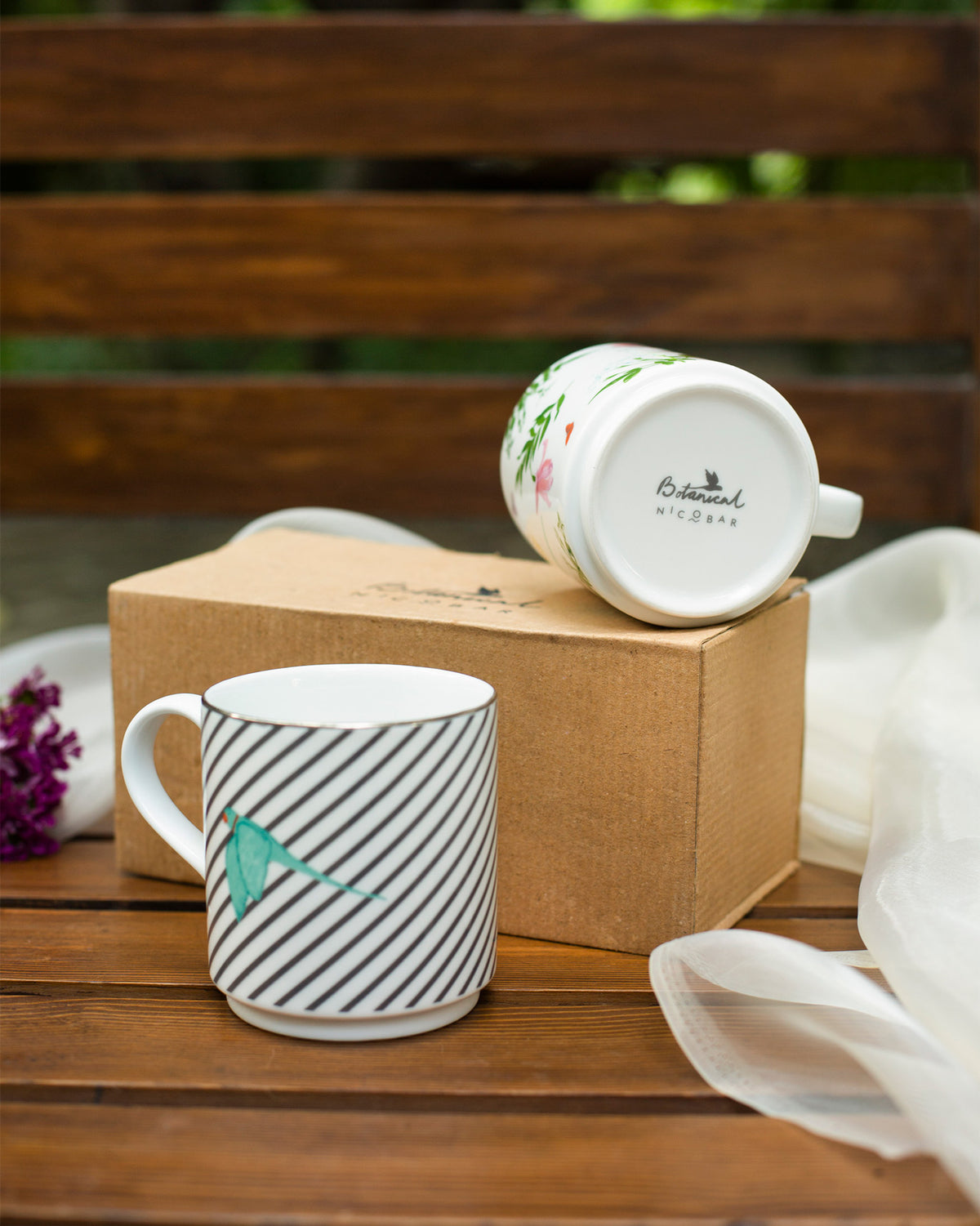 Striped Tota Mug beside a botanical Tota Mug tipped upside down on a cardboard box.