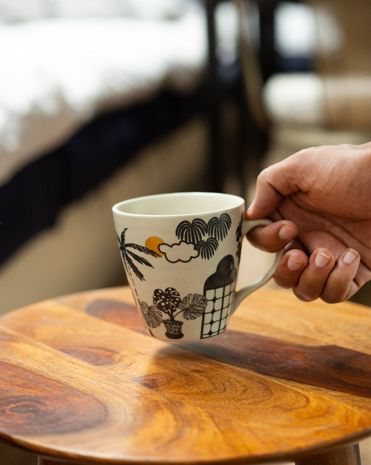 Person holding a Mandovi Palm Mug by its handle, with a sun on the print.