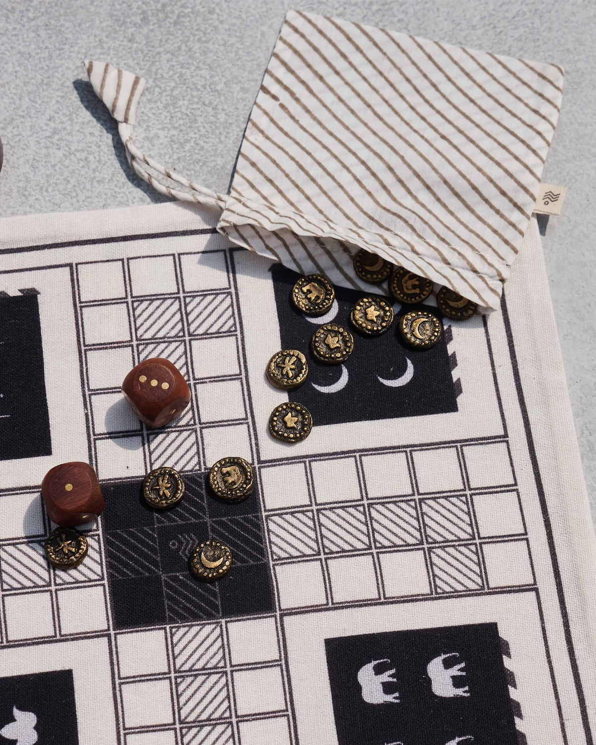 Nico Ludo drawstring pouch with brass tokens spilling onto the cloth board.