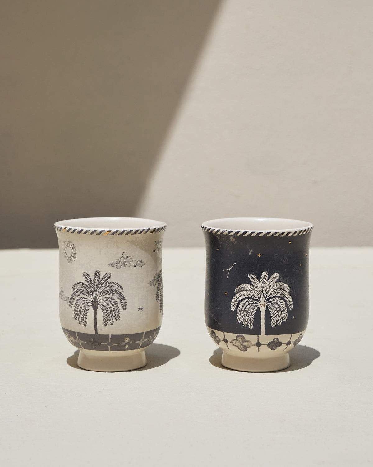 Pair of Twilight Tea Cups, one cream and one navy, each with a palm tree motif.