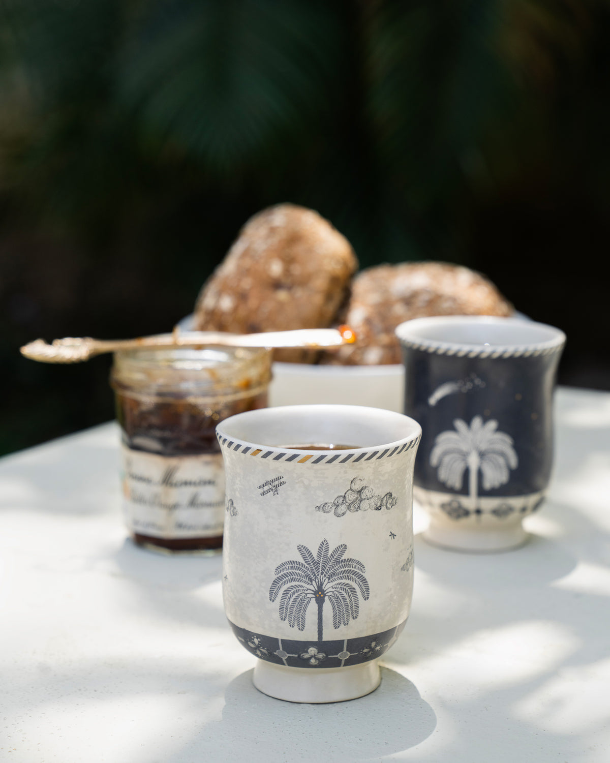Cream Twilight Tea Cup with a palm tree motif in front of a navy one.