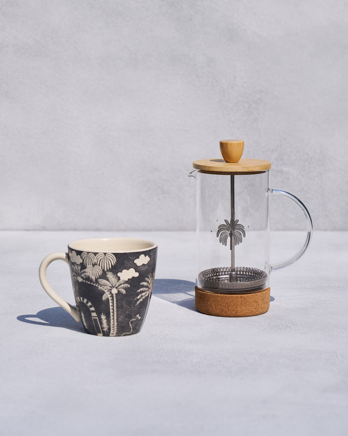Toddy French press with cork base and wooden lid beside a palm-print mug.
