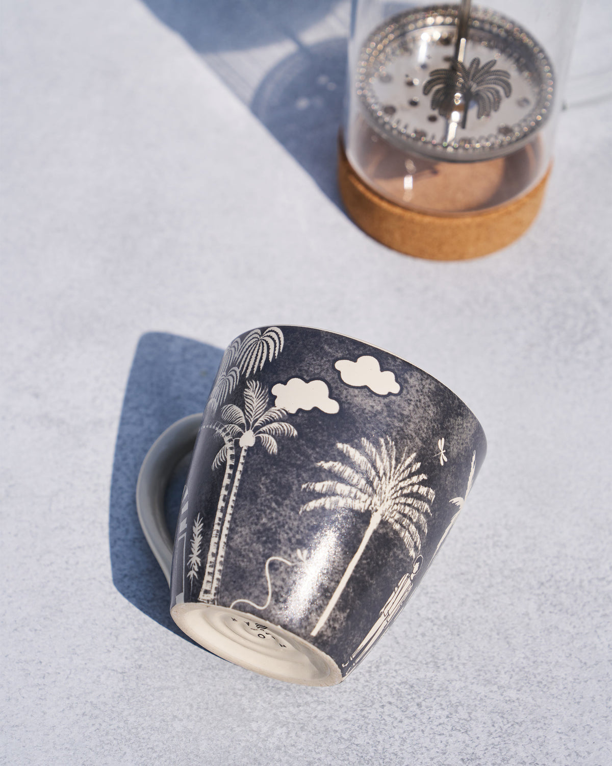 Charcoal Toddy mug with palm trees tipped toward a cork-base French press.